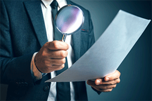 Someone wearing a suit and tie looks through a magnifying glass at a sheet of paper