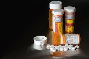 A collection of prescription drug bottles, one open with tablets spread out on a table.