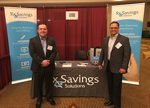Two Rx Savings Solutions employees stand in front of the company booth during the Pharmacy Benefit Management Institute conference