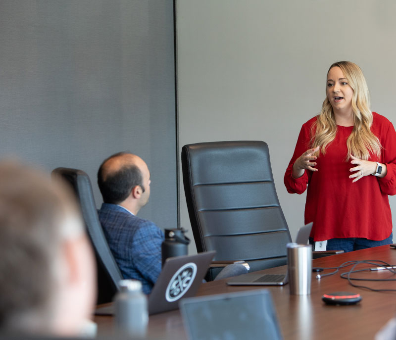 A woman standing up and giving a presentation at a conference room table