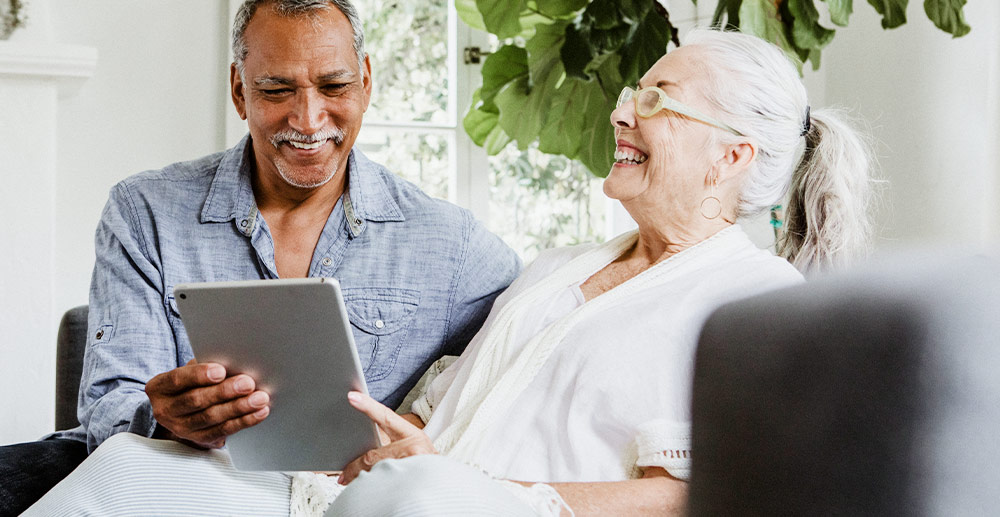 An older man and woman looking a tablet device and smiling